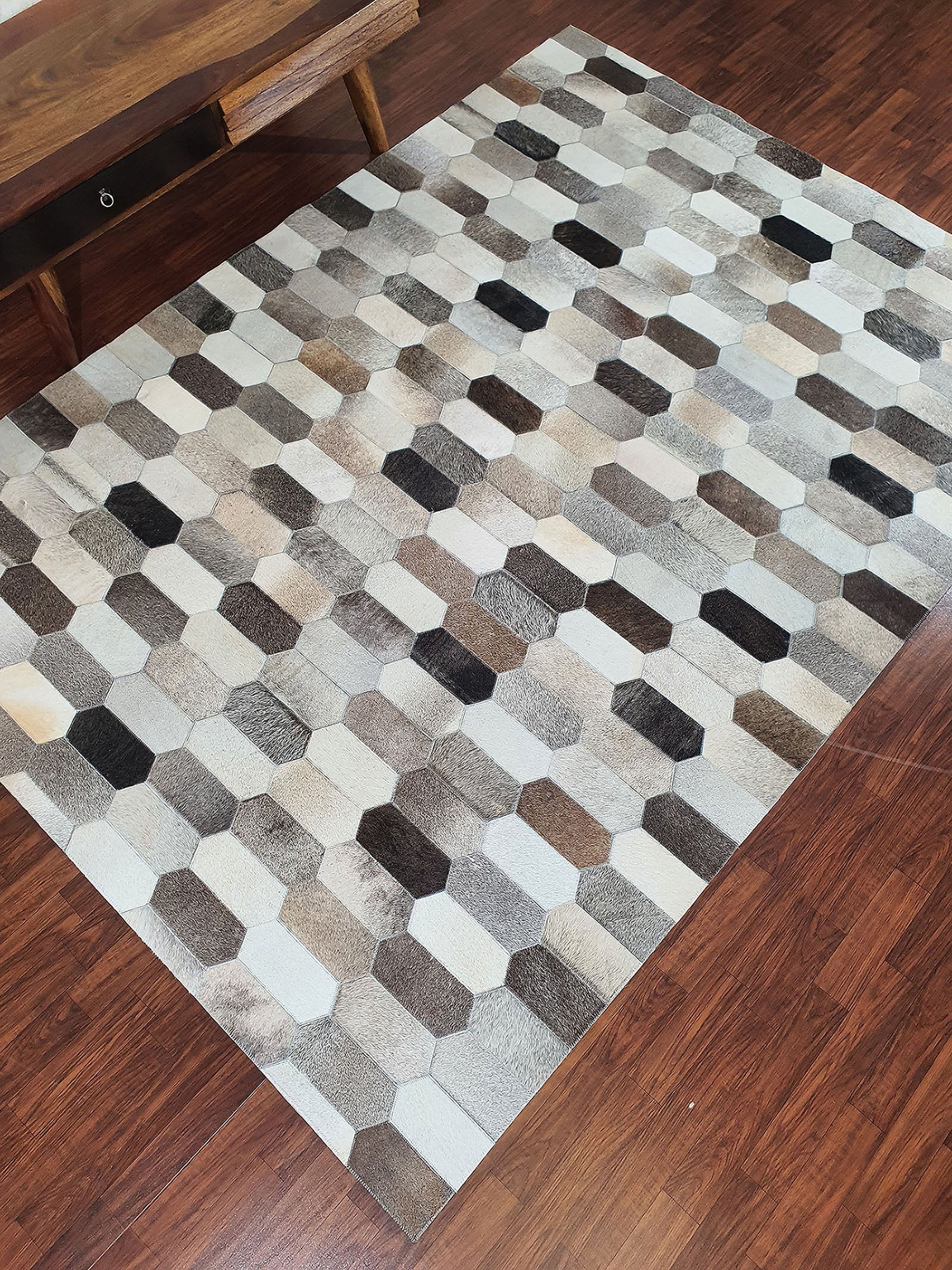 The RAMSHA HOME Multi Color Home Decor Leather Rug - LR 011, featuring a rectangular hexagon pattern in gray, beige, and brown, is placed on a wooden floor near a bench and adds modern style to the room.
