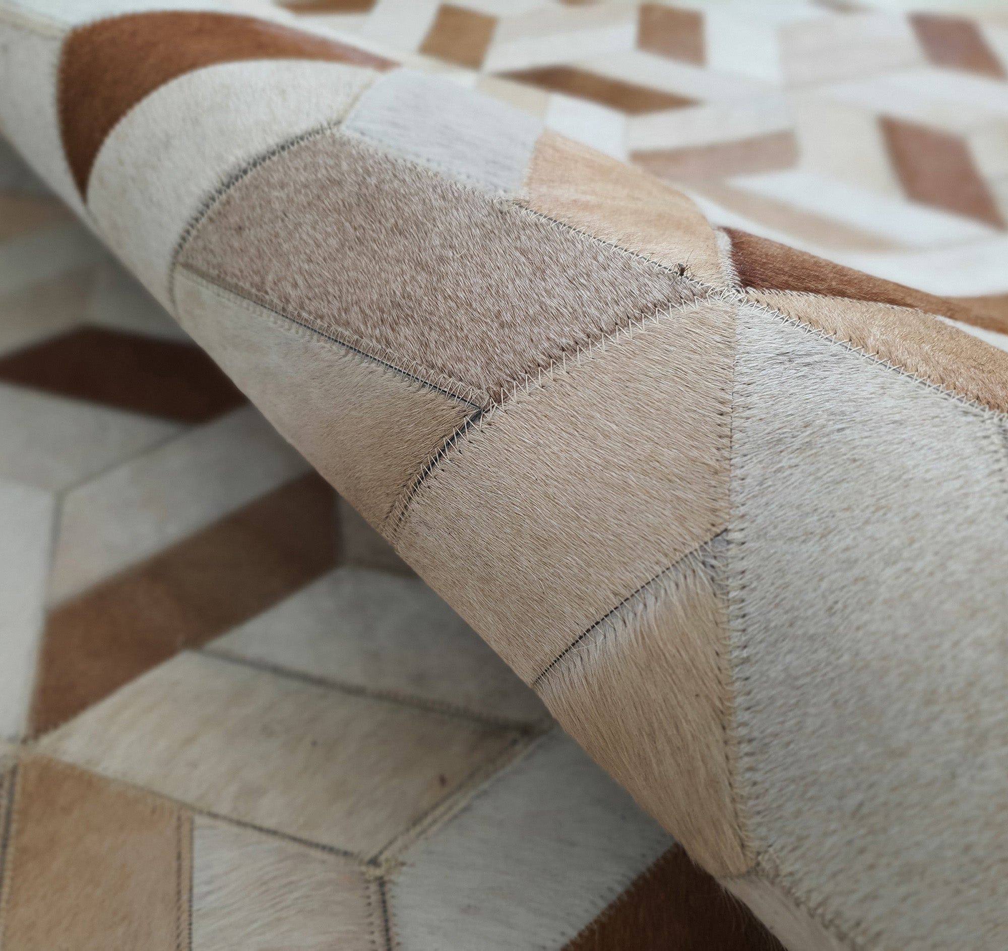 A close-up of the RAMSHA HOME Geometric Cube Pattern Handmade Leather Area Rug LR-012, featuring stitched tan and cream leather patches, with part of the patchwork rug rolled up.