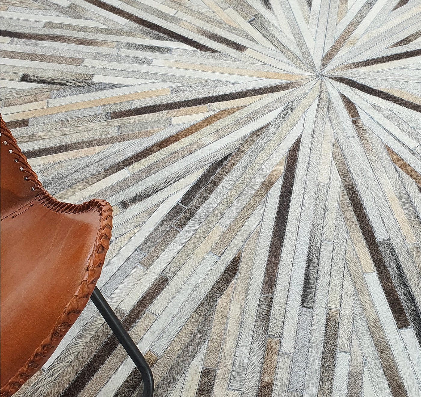 A close-up of the RAMSHA HOME Home Decorative Leather Rug - LR 018 shows radiating strips in a starburst pattern, with the corner of a stitched leather and metal chair visible in the lower left.
