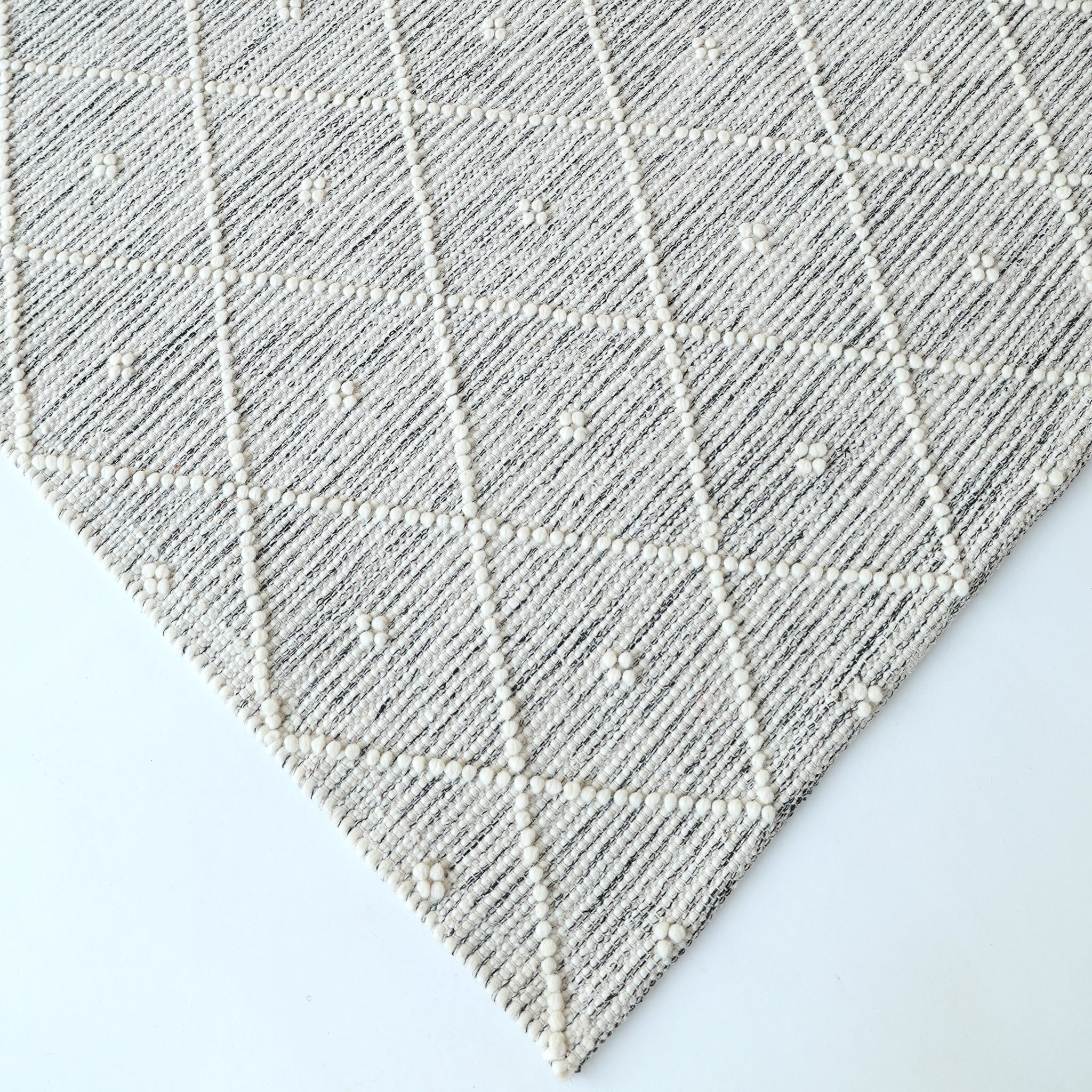 A close-up of the RAMSHA HOME Natural & White Color Woven Rug (SRN-012), featuring a subtle diamond and dot pattern with raised textured lines and small tufts, displayed on a white surface.