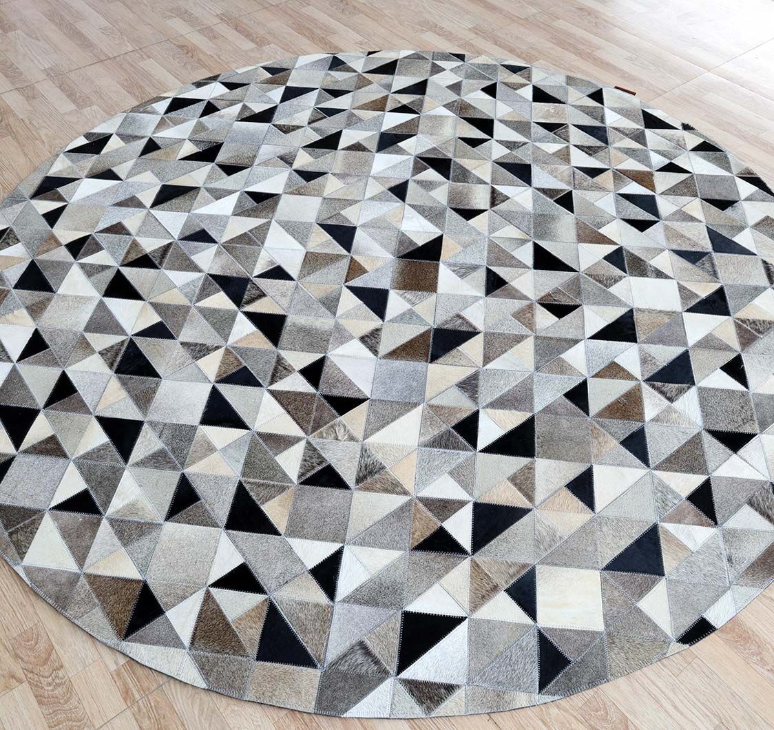 The Multi Color Home Decor Leather Rug - LR 020 by RAMSHA HOME features a round geometric pattern with triangles in black, white, gray, and brown, displayed on a light wood floor.