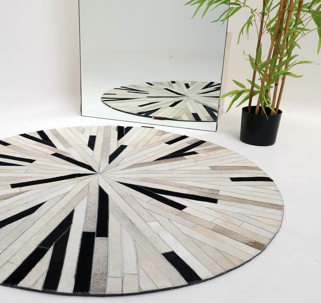 The Stunning Multi Color Dining Room Decor Leather Rug - LR 021 by RAMSHA HOME, featuring a geometric sunburst pattern in white, beige, and black, is placed on a white floor beside a tall green plant and a large mirror reflecting the scene.