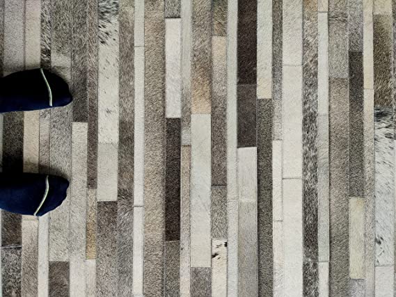 Two sock-covered feet stand on a floor with the RAMSHA HOME Grey Color Kitchen Decor Leather Rug - LR 004, featuring staggered rectangular tiles in shades of gray and beige.