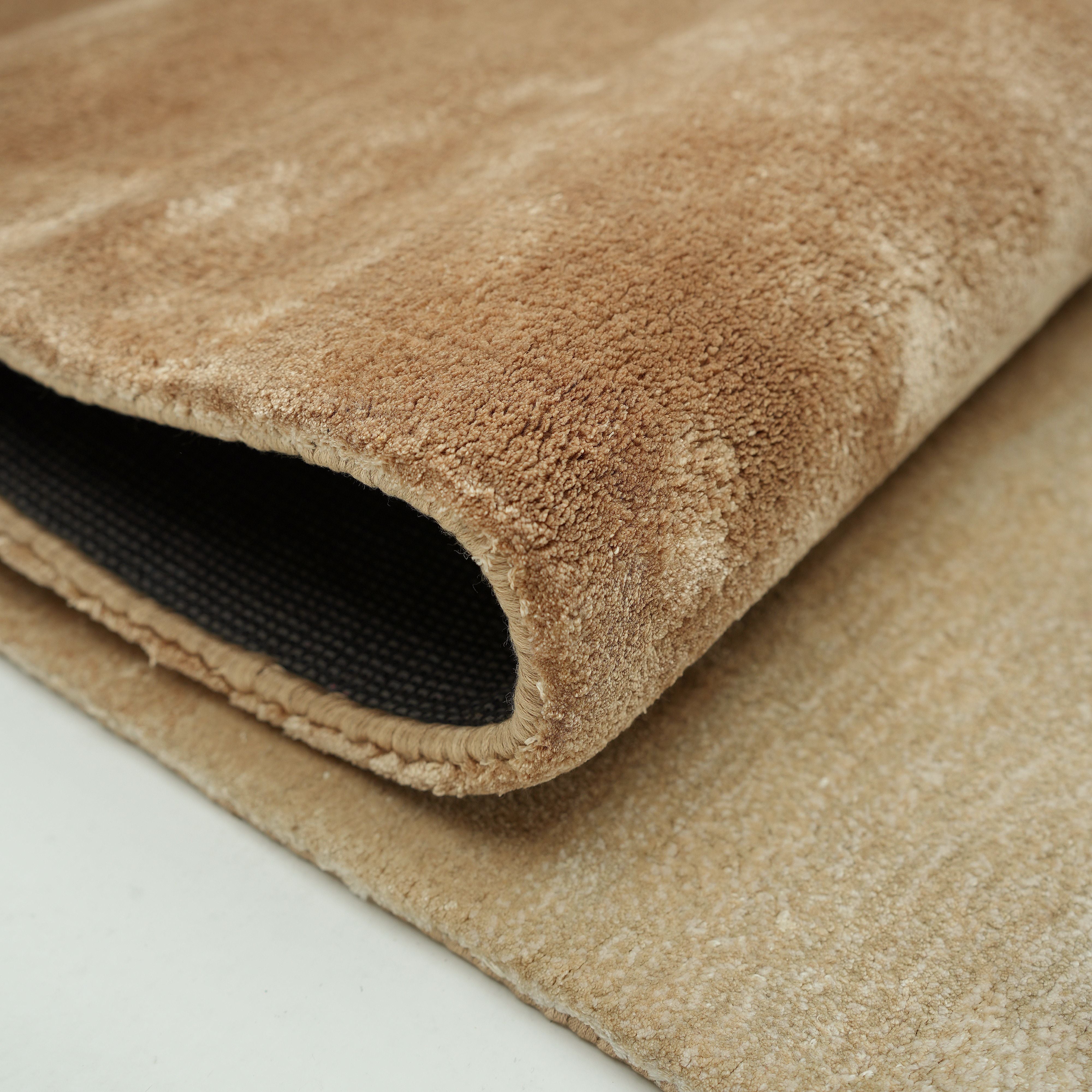 Close-up of the Caramel Ombre Handmade Area Rug - HTV 26 (300X400 cm) by RAMSHA HOME, showing its plush beige hand-tufted surface partially rolled to reveal the textured underside on a light floor.