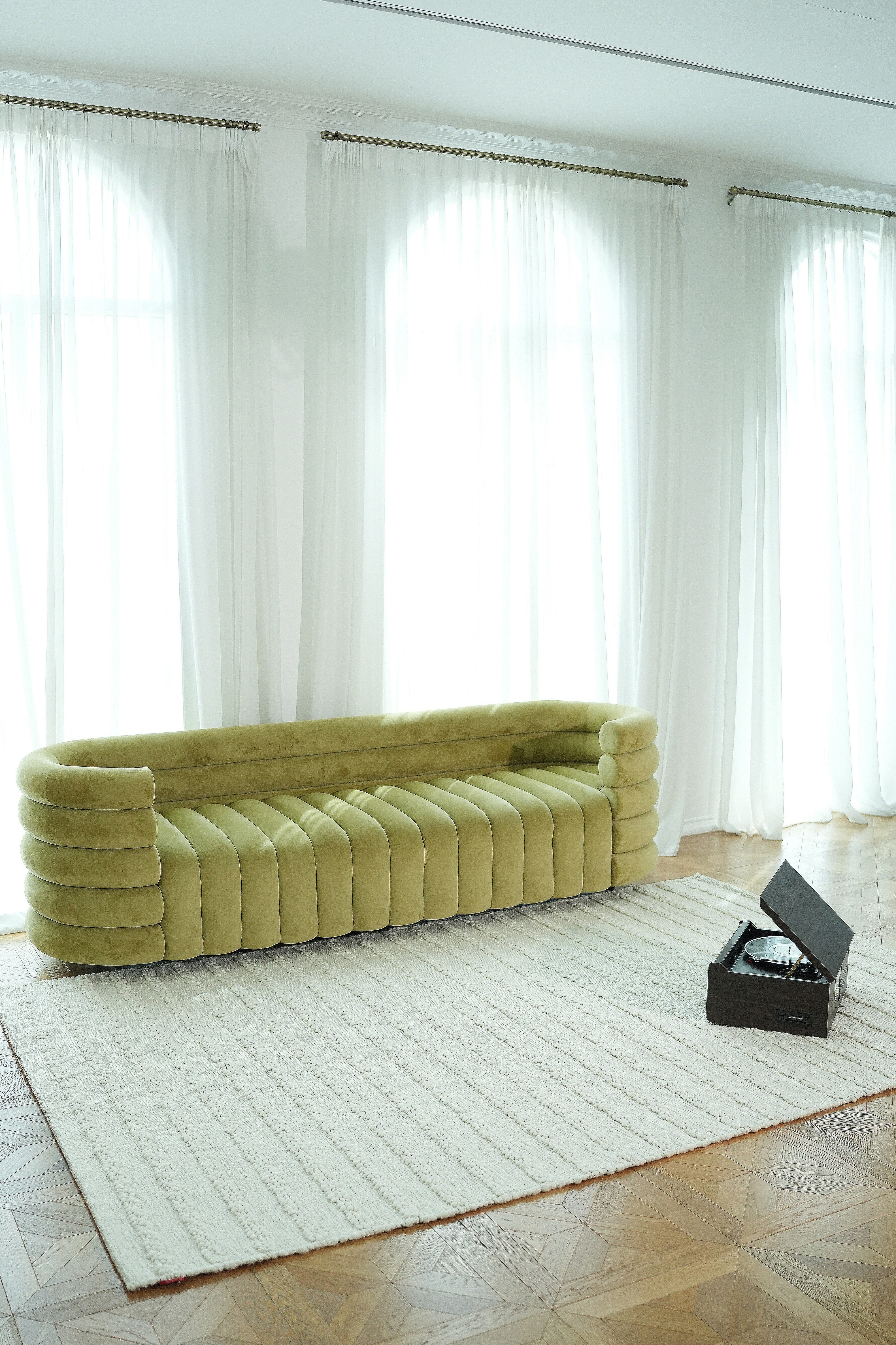 A modern living room with sheer white curtains, a long green velvet sofa, and a RAMSHA HOME Home Decor Woven Rug Natural Color Bedroom Rug SRN-037, plus a black open record player on the floor.