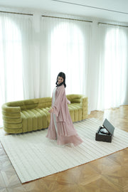A woman in a flowing pink dress stands on the RAMSHA HOME Home Decor Woven Rug Natural Color Bedroom Rug SRN-037 in front of a green sofa, with sheer white curtains behind her and an open record player to her right.