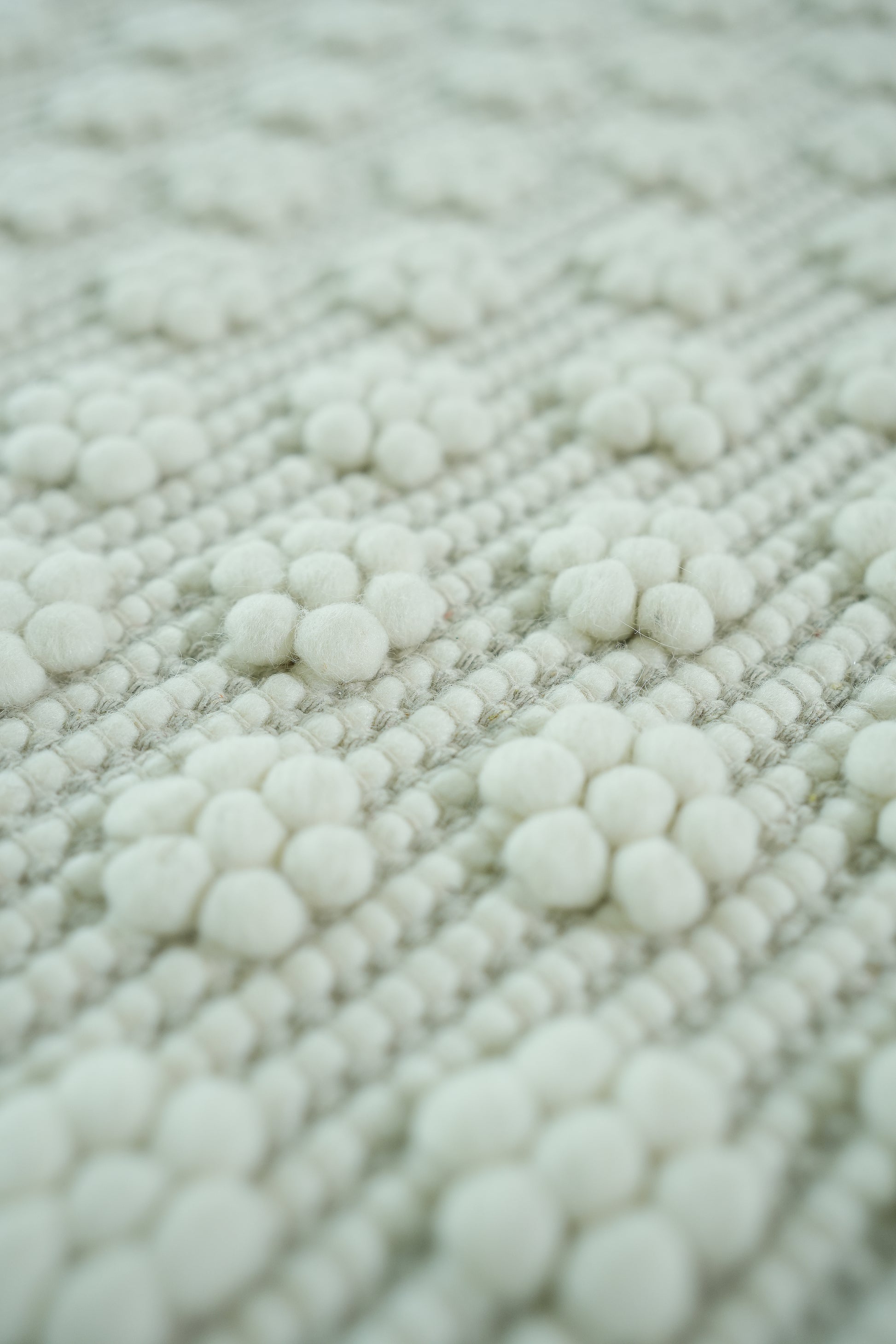 A close-up of the RAMSHA HOME Home Decor Woven Rug Natural Color Area Rug SRN-038, featuring a textured surface with soft, round, white woolen balls in a floral pattern on its neutral background.