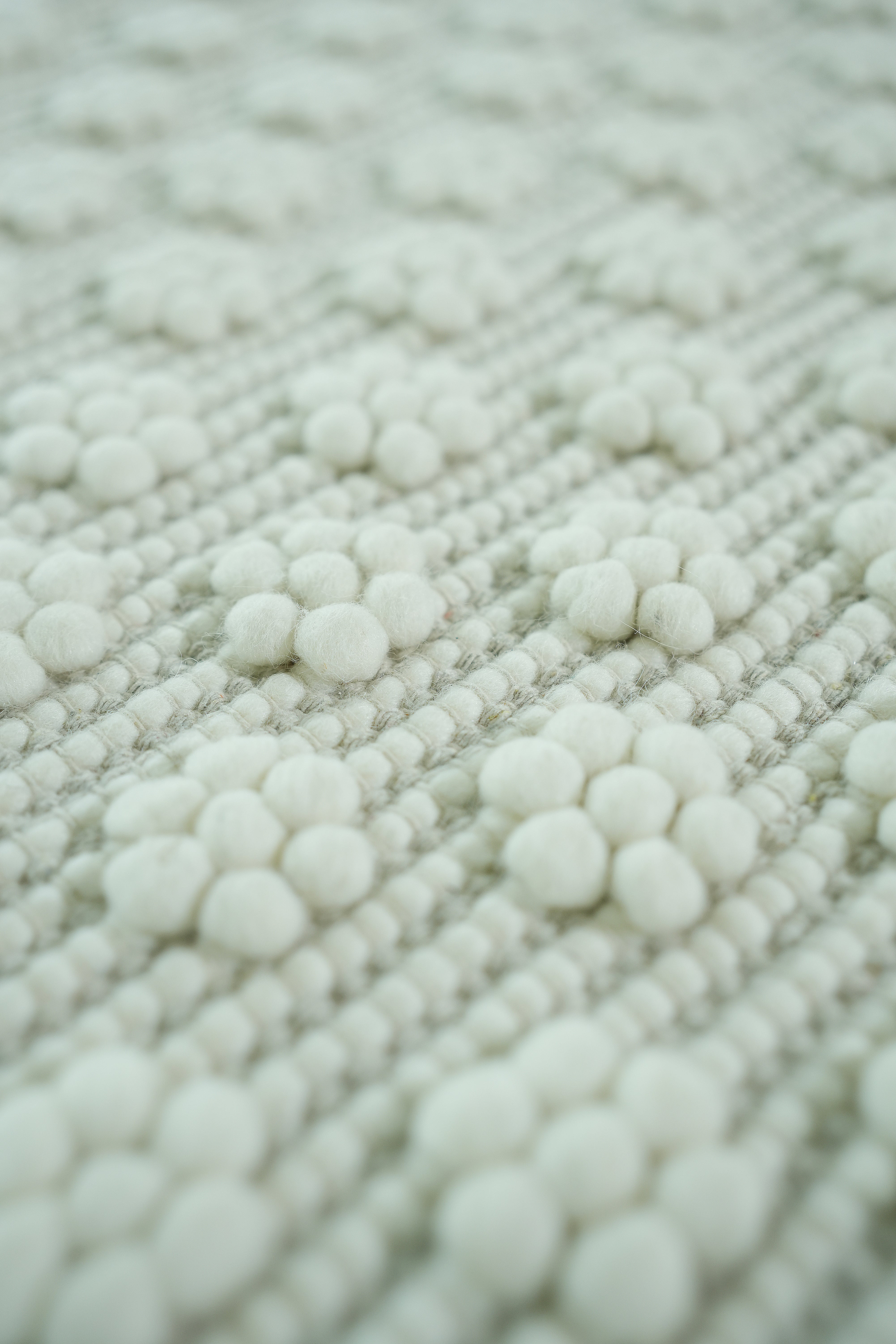 A close-up of the RAMSHA HOME Home Decor Woven Rug Natural Color Area Rug SRN-038, featuring a textured surface with soft, round, white woolen balls in a floral pattern on its neutral background.