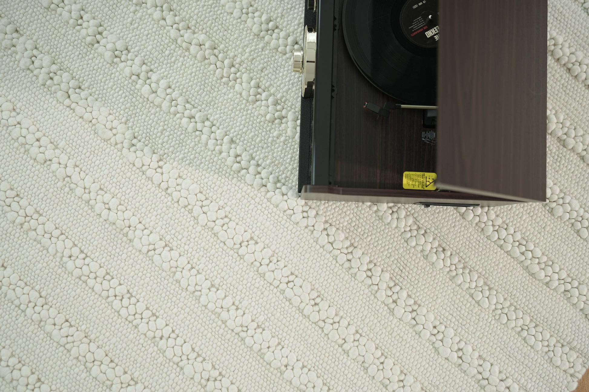 A top-down view shows a record player playing vinyl on the right, placed on the RAMSHA HOME Home Decor Woven Rug Natural Color Bedroom Rug SRN-037 with a white patterned surface.