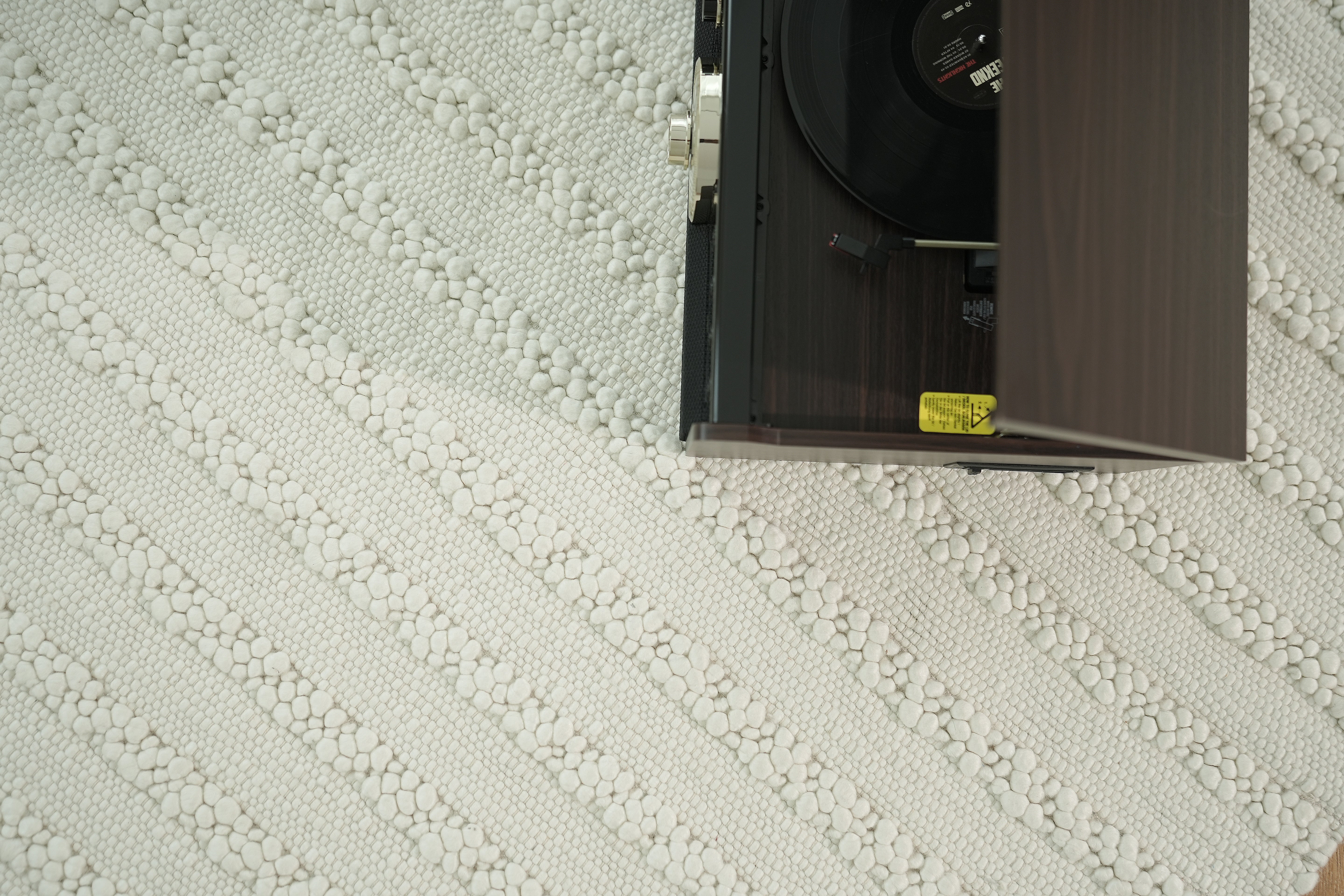 A top-down view shows a record player playing vinyl on the right, placed on the RAMSHA HOME Home Decor Woven Rug Natural Color Bedroom Rug SRN-037 with a white patterned surface.