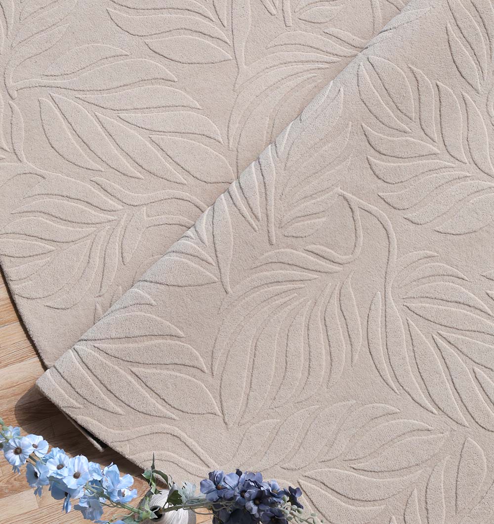 The RAMSHA HOME Premium Off-White Area Carpet - HTW 115 (200x300 cm) is shown partially folded on a wooden floor, accented with sprigs of light blue and purple flowers.