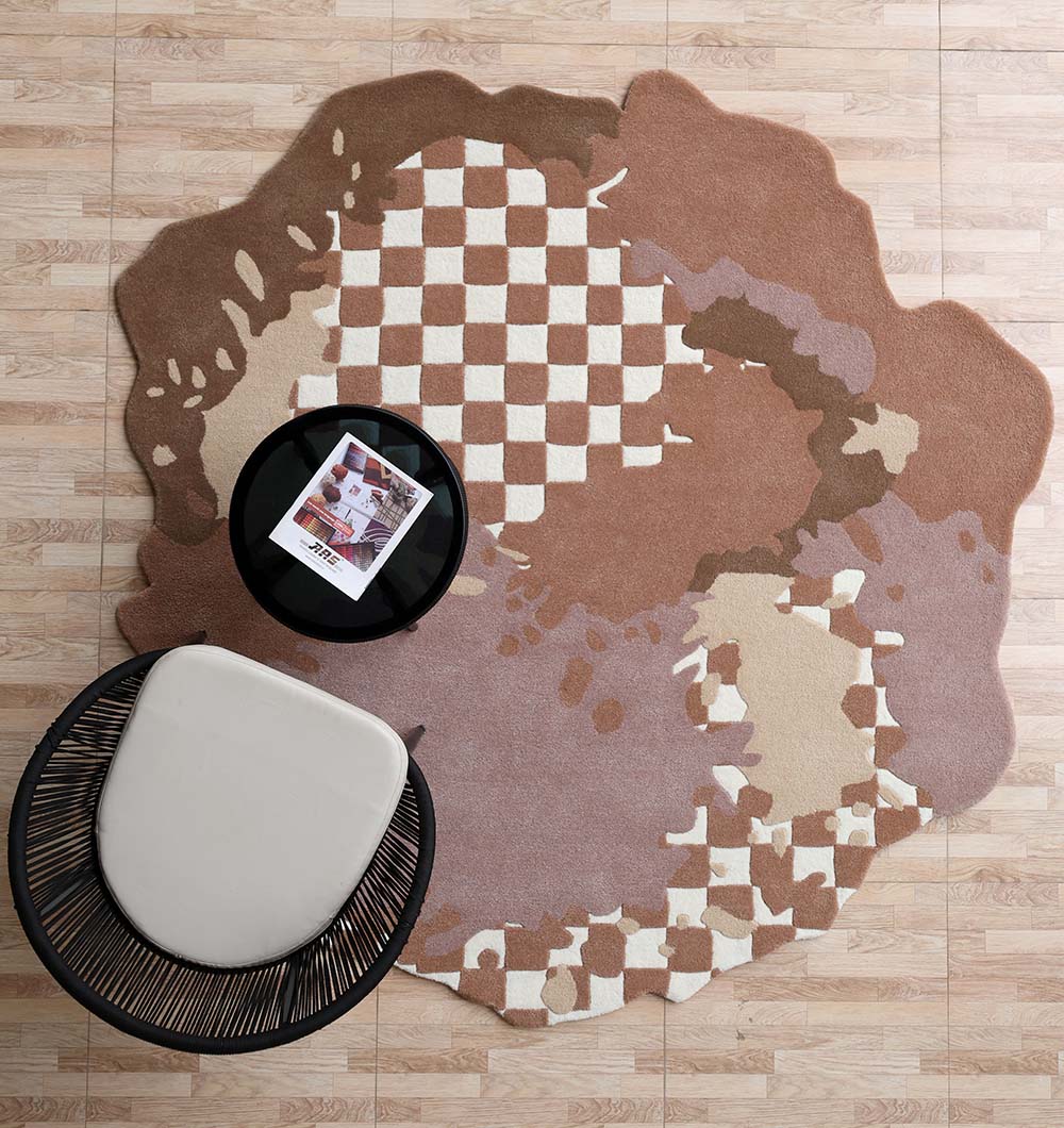 The Handmade Multicolor Area Bespoke Rug HTW 128 (200cm) by RAMSHA HOME, with a beige, brown, and cream checkered design, sits on a wooden floor under a black round table with a magazine and a modern white chair.