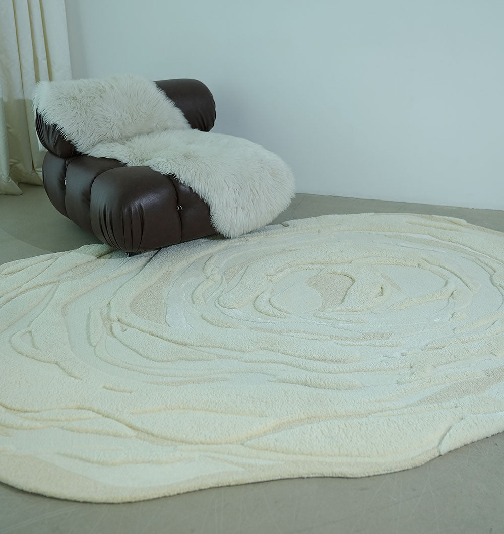 A dark brown modern armchair with a white faux fur throw sits beside the RAMSHA HOME Beige Color Oval Shaped Handmade Rug - HTWV 106 (200x300cm) on a light gray floor against a plain white wall.