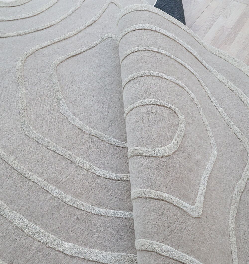 The RAMSHA HOME Beautiful Off White Handmade Rug (HTWV-112, 200x300cm) features hand-tufted, raised wavy lines and a textured tencel-wool blend, elegantly displayed on a wooden floor with its thickness partially revealed.