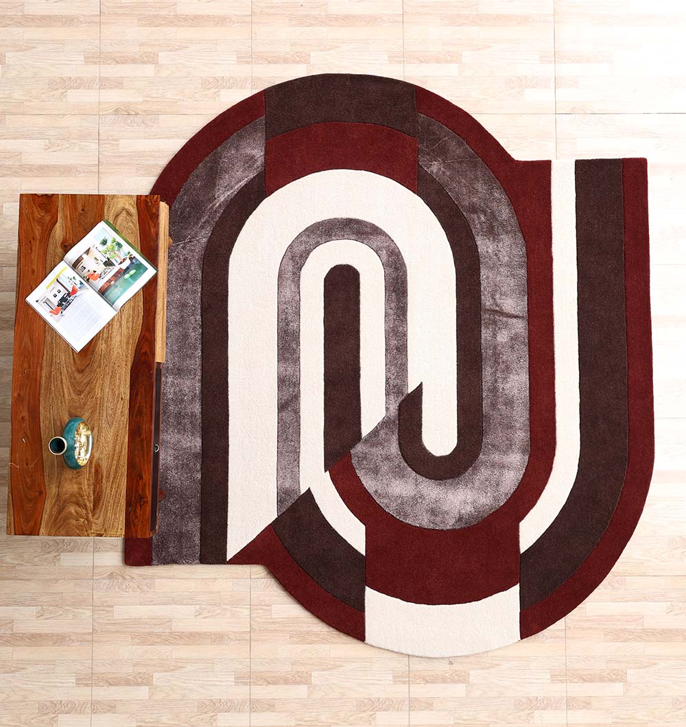 A wooden coffee table with an open magazine and cup sits beside the RAMSHA HOME Modern Geometric Shaped Rug HTWV 184 (200 x 226 cm), featuring maroon, brown, gray, and cream curves on a light wood floor.