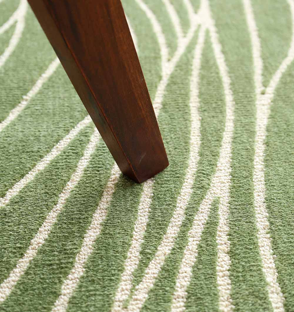 A wooden furniture leg rests on the RAMSHA HOME Leaf Vein Line Pattern Green & Ivory Rug – KD 015, featuring abstract white lines on a green background.