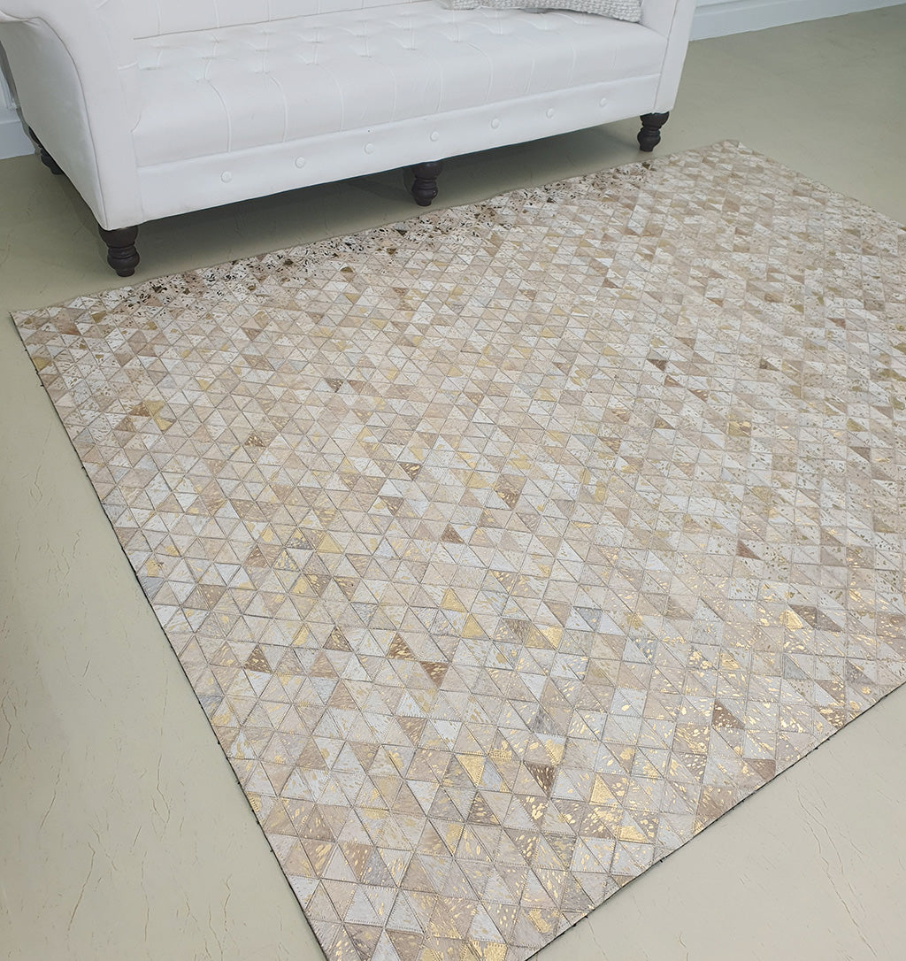 The Amazing Grey & Tan Color Playroom Leather Rug - LR 006, featuring a geometric patchwork design, lies in front of a white tufted sofa with dark wooden legs in a bright, modern room.