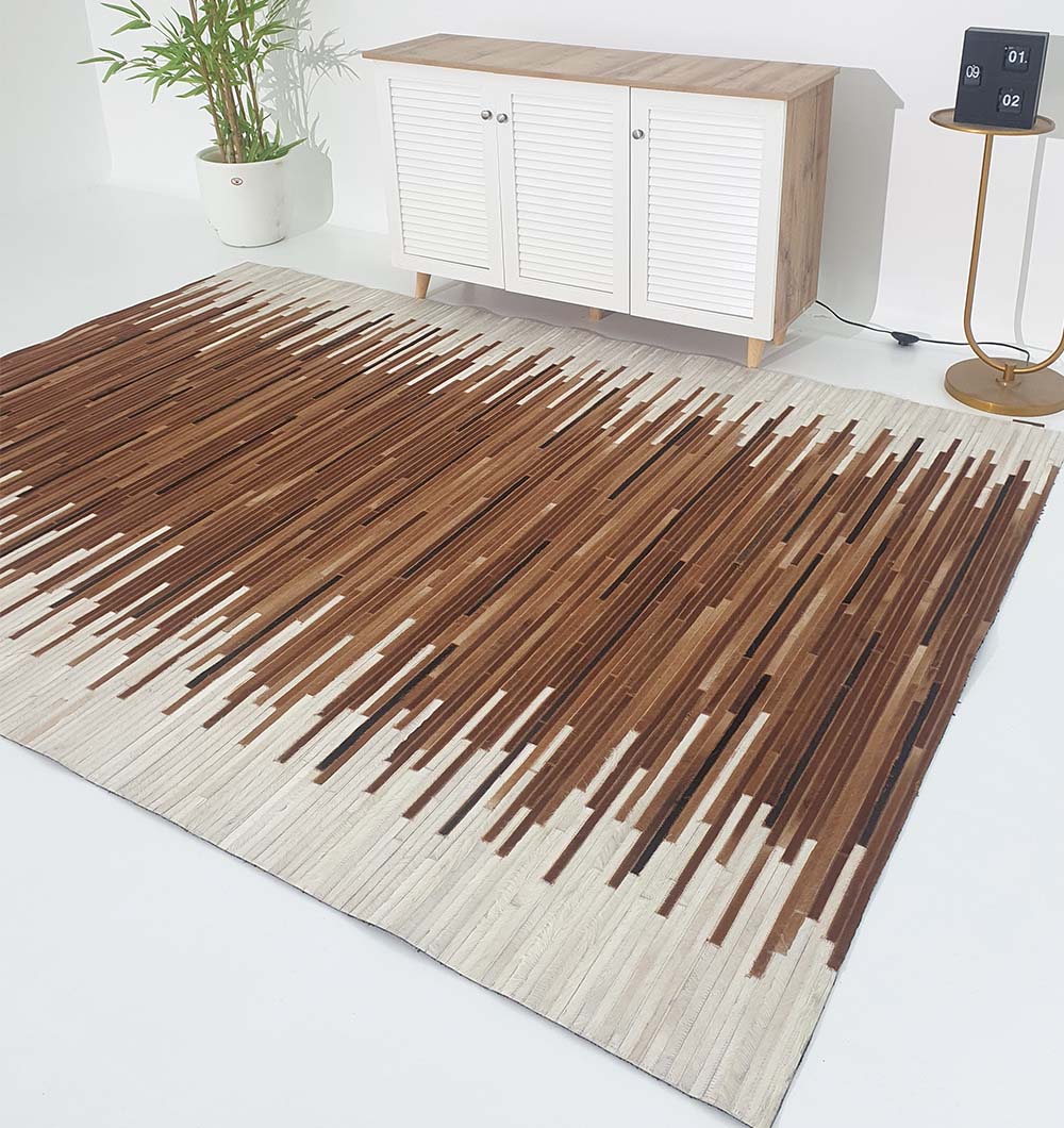 A bright modern living room features the RAMSHA HOME Handmade Multi-Color Leather and Wool Area Rug LR-014 in beige and brown, a white cabinet with wooden top, a potted plant, and a round side table with a digital calendar. Minimal decor completes the space.