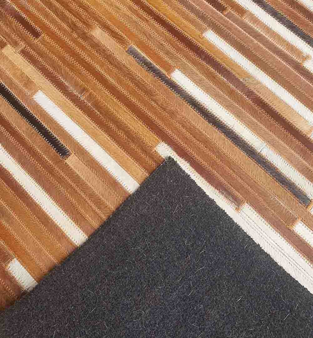 A dark abrasive pad is placed on a wooden floor next to the RAMSHA HOME Handmade Multi-Color Leather and Wool Area Rug LR-014, which features brown and cream stripes.