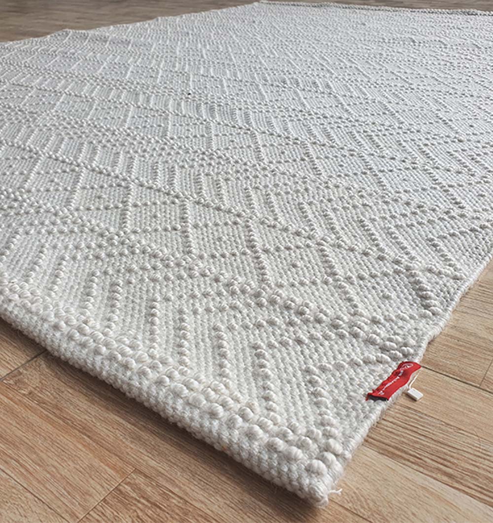 A close-up of the RAMSHA HOME White Rectangle Woven Area Rug and Carpet for Living Room, Bedroom (SR-022), crafted from durable polyester with geometric patterns, off-white tone, and a small red fabric tag on one corner.