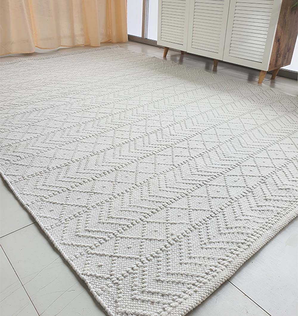 The RAMSHA HOME White Rectangle Woven Area Rug And Carpet For Living Room, Bedroom SR-022 adds a light, modern touch with its textured geometric pattern to a bright room featuring tiled floors, sheer curtains, and a white cabinet.