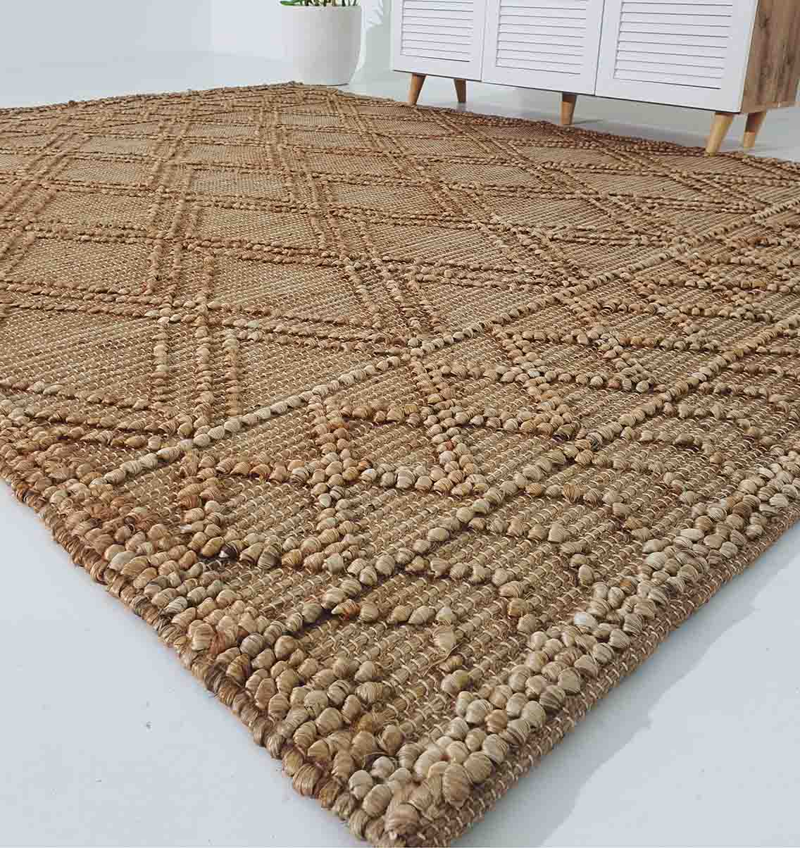 A close-up of the RAMSHA HOME Floor Woven Living Room Rug (Natural Color, Rectangle, SR-019) shows its textured geometric diamond patterns, placed on a light floor beside a white cabinet with wooden legs.