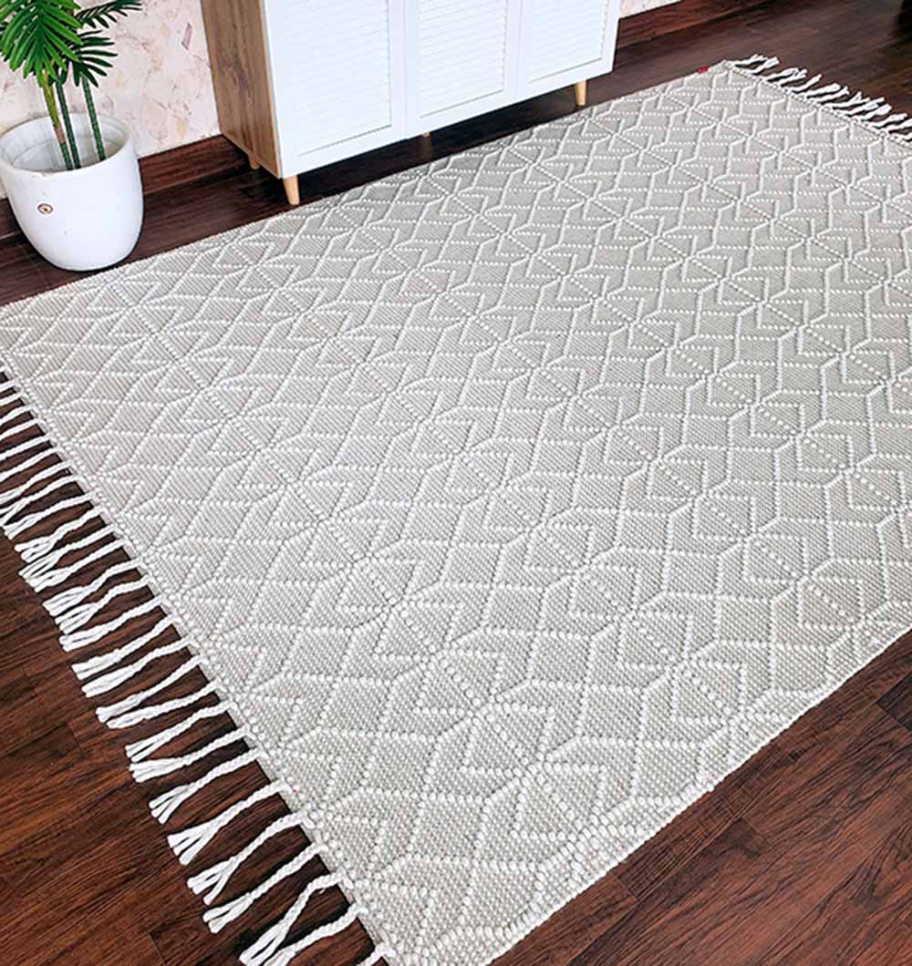 The RAMSHA HOME Handmade Woven Rug (Natural White, Fringes Decor, SRN-007) features a light diamond pattern and tassels, placed on a dark wooden floor near a white cabinet and potted plant.