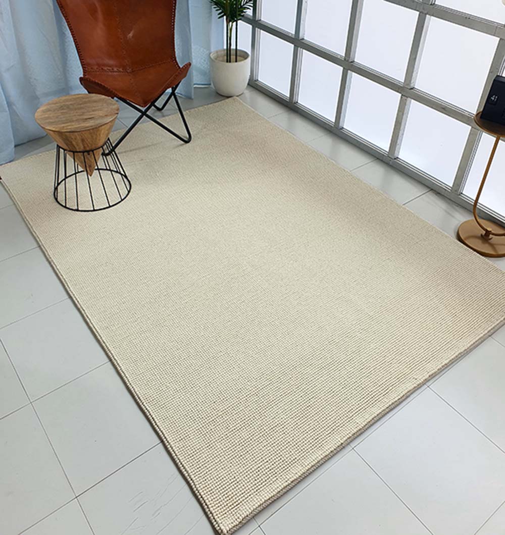 A modern room with a Solid Loop Pile Woven Rug For Home Decor SRN-032 in beige, a brown leather chair, a small wooden side table with metal legs, a potted plant, and large frosted windows letting in natural light.