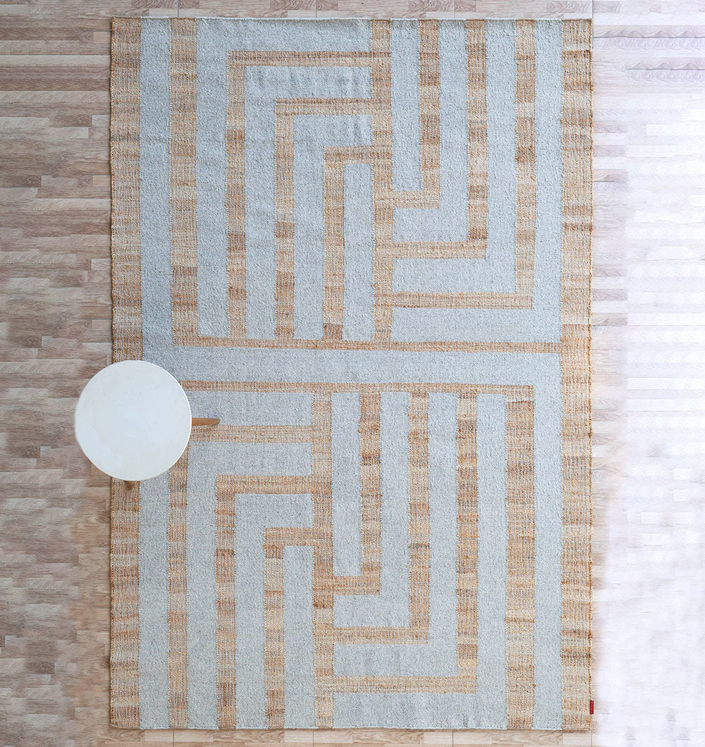 The Jute & Wool Natural Color Hand Woven Rug WR-036 by RAMSHA HOME lies on a light wooden floor, complemented by a small round white table placed on the left side.